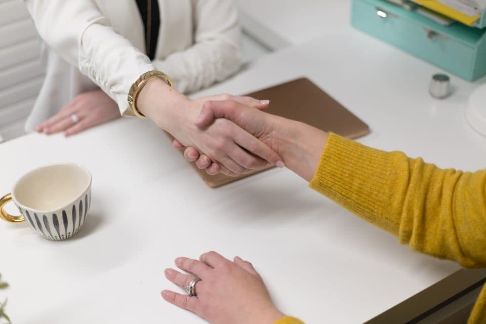 Two people shaking hands across a desk after reaching an agreement